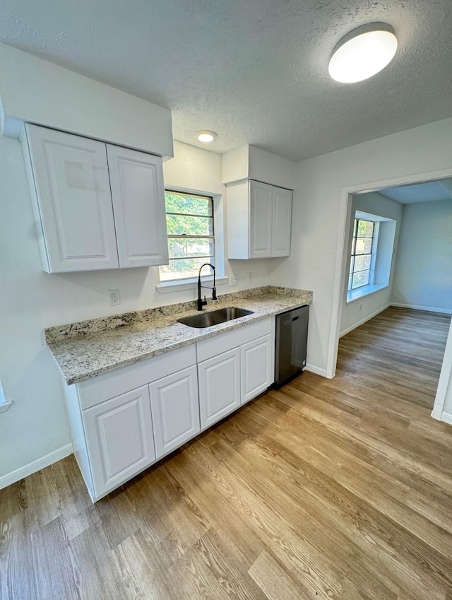 7810 Bunker Wood Ln, Houston, TX 77086 - kitchen with light wood-style flooring, a sink, white cabinets, baseboards, and dishwasher