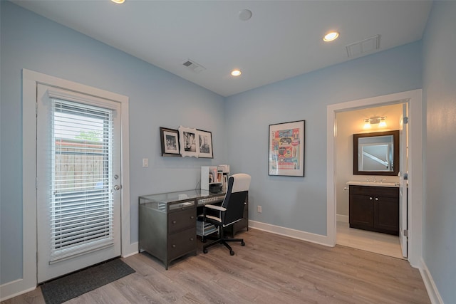office with baseboards, visible vents, a sink, and light wood finished floors