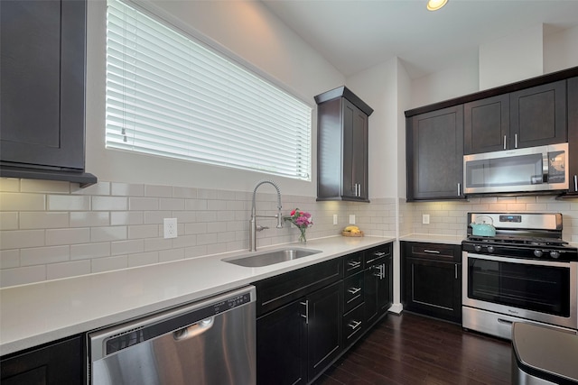kitchen with appliances with stainless steel finishes, a sink, light countertops, dark wood finished floors, and backsplash