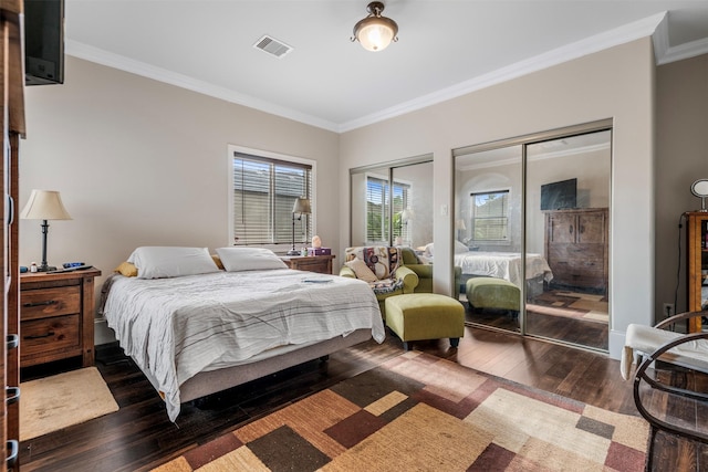 bedroom with visible vents, multiple closets, crown molding, and hardwood / wood-style flooring