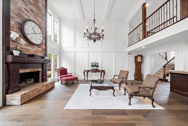 living area featuring a brick fireplace, wood finished floors, a decorative wall, a high ceiling, and stairway