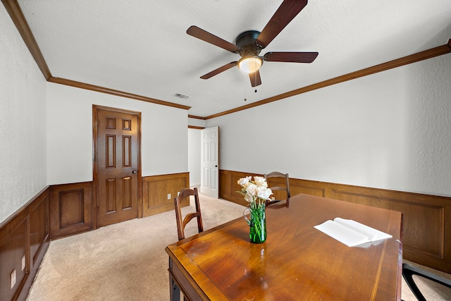dining space featuring crown molding, ceiling fan, light colored carpet, wainscoting, and visible vents