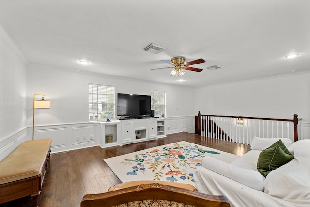 living room featuring ceiling fan, a decorative wall, dark wood-type flooring, visible vents, and ornamental molding