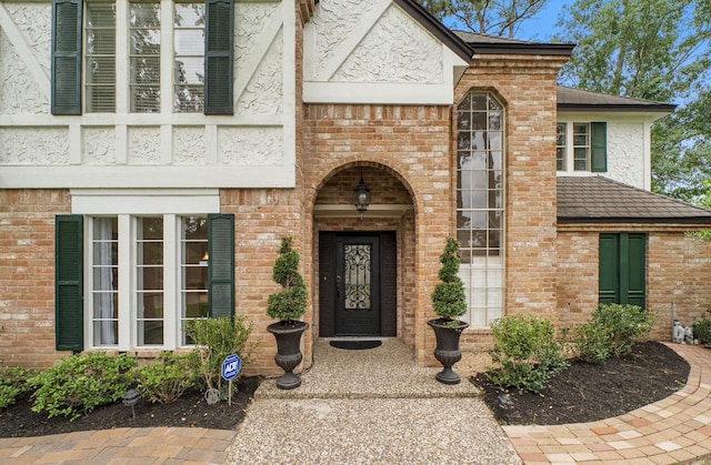 view of exterior entry with a shingled roof, stucco siding, and brick siding