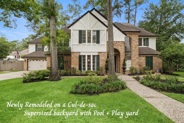 tudor home with a garage, fence, a front yard, brick siding, and driveway