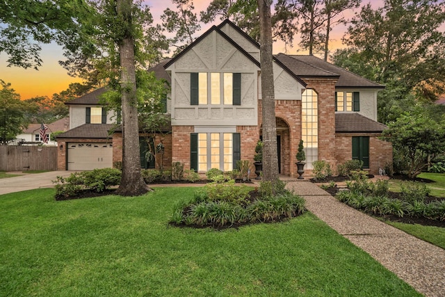 tudor home featuring a lawn, fence, concrete driveway, and brick siding