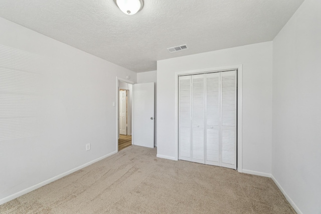 unfurnished bedroom with visible vents, a closet, baseboards, a textured ceiling, and carpet