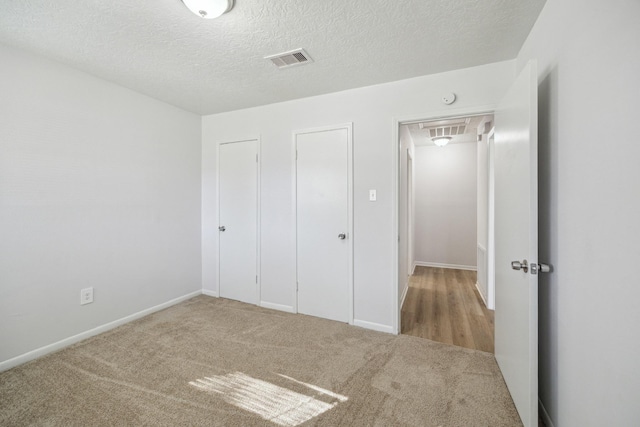 unfurnished bedroom featuring carpet floors, a textured ceiling, visible vents, and baseboards