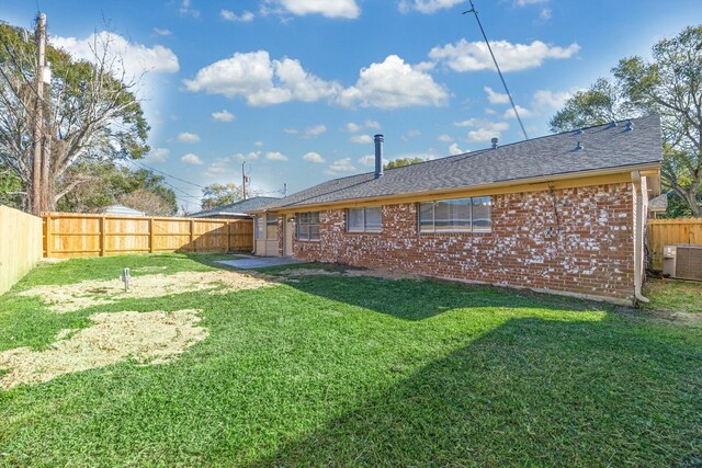 back of property with cooling unit, a fenced backyard, roof with shingles, brick siding, and a lawn