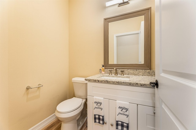 half bath featuring vanity, baseboards, toilet, and wood finished floors