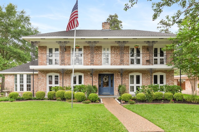 colonial inspired home featuring brick siding, a front yard, a chimney, and a balcony