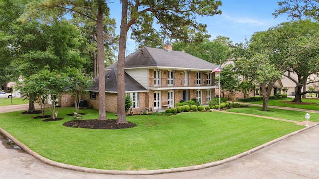view of front of house with a balcony, a chimney, brick siding, and a front lawn