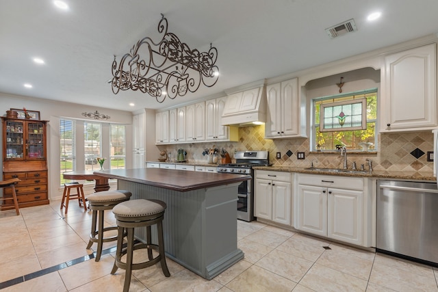 kitchen with custom exhaust hood, visible vents, a sink, backsplash, and stainless steel appliances