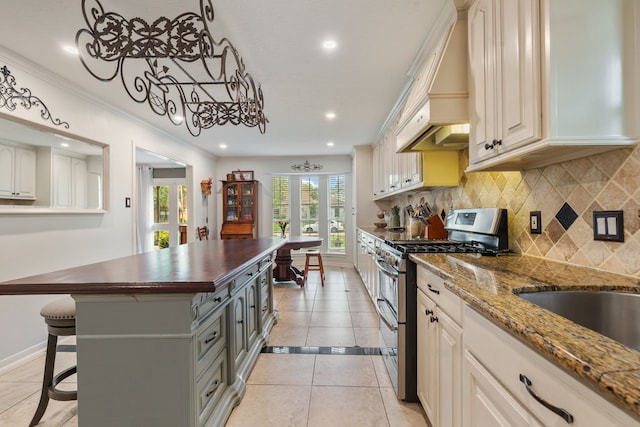 kitchen with butcher block countertops, range with two ovens, light tile patterned flooring, premium range hood, and tasteful backsplash