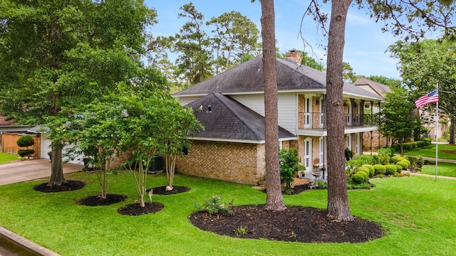 view of front of property featuring a balcony, a front yard, brick siding, and a chimney