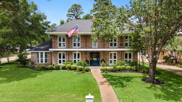 view of front facade featuring a balcony, a front yard, brick siding, and covered porch