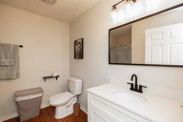 bathroom featuring a shower with shower door, vanity, toilet, baseboards, and wood finished floors
