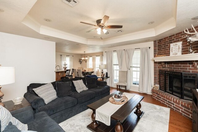 living room with visible vents, ornamental molding, wood finished floors, a raised ceiling, and ceiling fan with notable chandelier