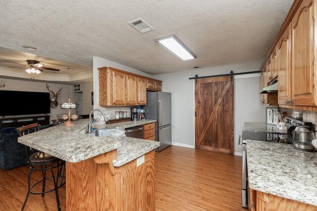 kitchen with appliances with stainless steel finishes, light wood-type flooring, a barn door, a peninsula, and under cabinet range hood