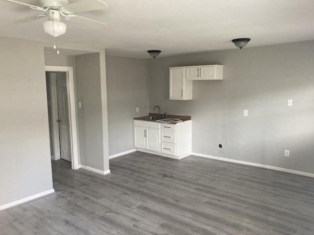 interior space featuring ceiling fan, dark wood-style flooring, a sink, baseboards, and white cabinets