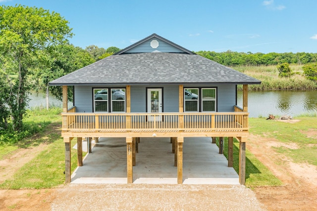 coastal home with a water view, driveway, roof with shingles, and a carport