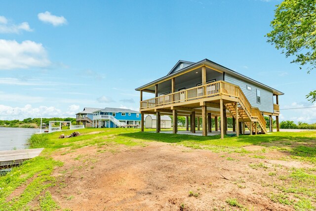 back of property featuring dirt driveway, stairs, a deck with water view, and a carport