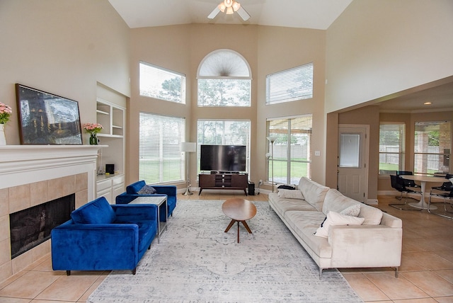living area featuring ceiling fan, built in features, a fireplace, a high ceiling, and light tile patterned flooring