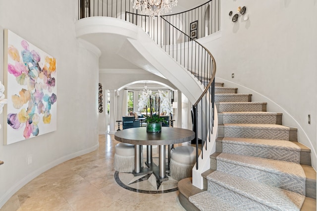 staircase with a high ceiling, a notable chandelier, arched walkways, baseboards, and ornate columns
