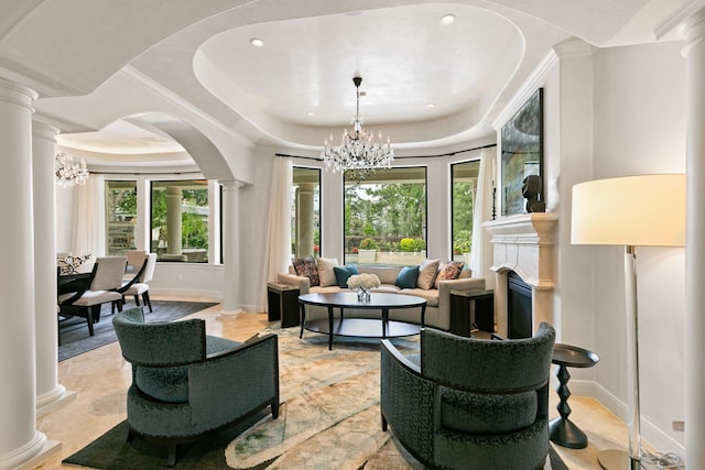 living area with arched walkways, decorative columns, a tray ceiling, and a notable chandelier