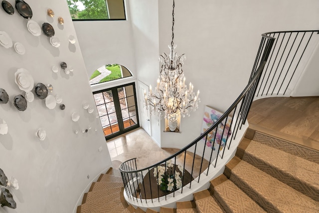 stairway featuring french doors, a towering ceiling, and a chandelier