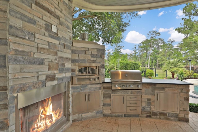 view of patio featuring an outdoor stone fireplace, fence, exterior kitchen, and area for grilling