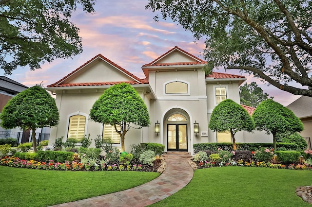 mediterranean / spanish home with a front lawn, stucco siding, french doors, and a tile roof