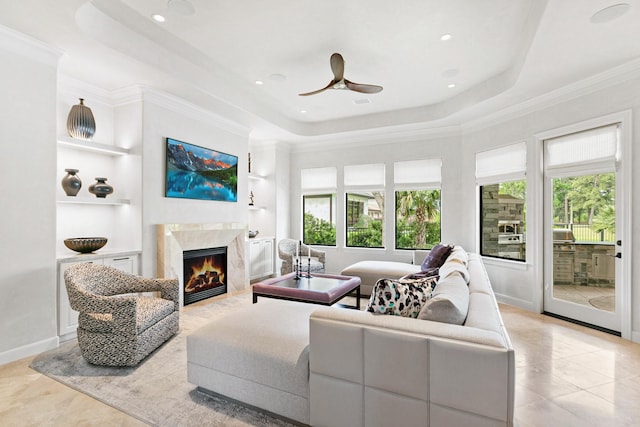 living area with crown molding, ceiling fan, a raised ceiling, built in features, and a high end fireplace
