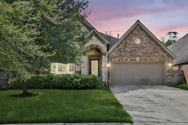 french provincial home with a lawn, brick siding, concrete driveway, an attached garage, and stone siding