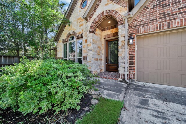 view of exterior entry featuring brick siding, fence, concrete driveway, an attached garage, and stone siding