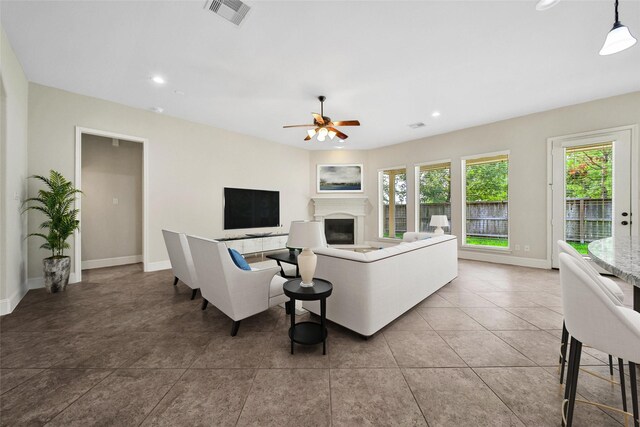 tiled living room with a fireplace with raised hearth, a ceiling fan, baseboards, recessed lighting, and visible vents