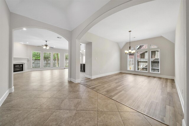 unfurnished living room featuring baseboards, vaulted ceiling, a glass covered fireplace, and ceiling fan with notable chandelier