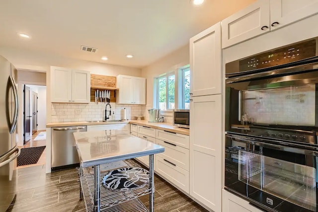 kitchen featuring visible vents, white cabinetry, tasteful backsplash, a sink, and stainless steel appliances