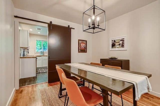 dining area featuring visible vents, baseboards, light wood-type flooring, a barn door, and a notable chandelier