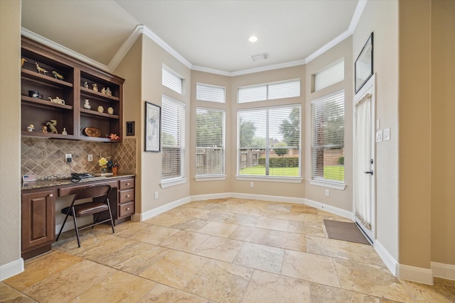 interior space featuring visible vents, crown molding, built in desk, baseboards, and stone tile floors