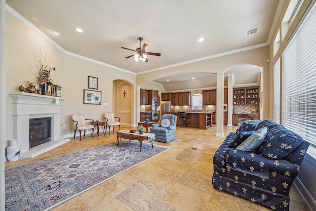 living room featuring crown molding, arched walkways, a ceiling fan, and visible vents