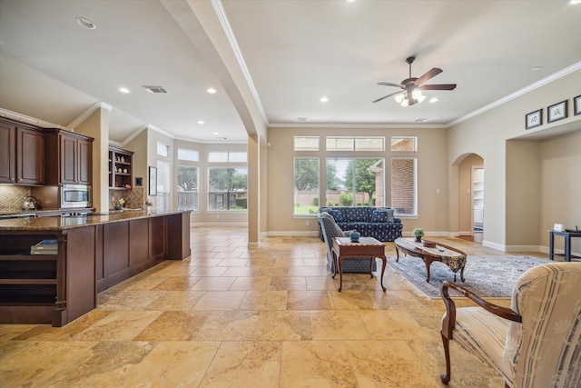 interior space featuring open shelves, ornamental molding, baseboards, open floor plan, and arched walkways