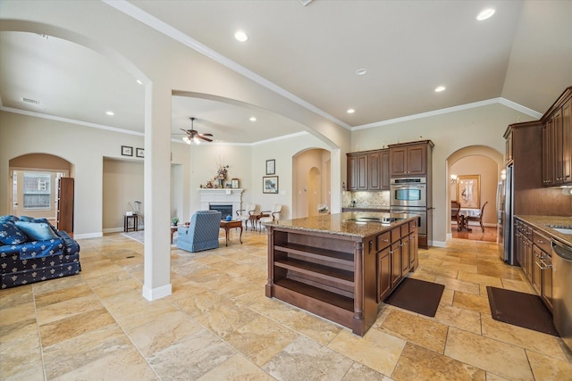 kitchen with stainless steel appliances, ceiling fan, an island with sink, and arched walkways