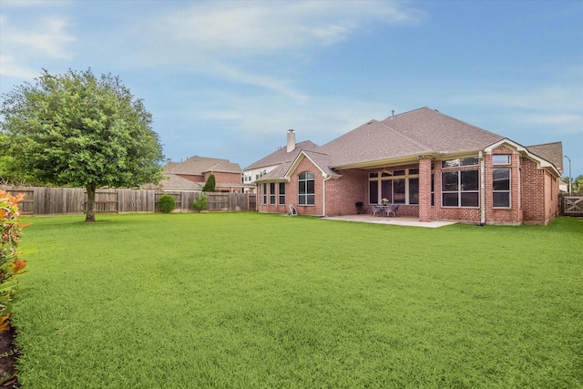 rear view of house with a lawn, a patio, brick siding, and a fenced backyard