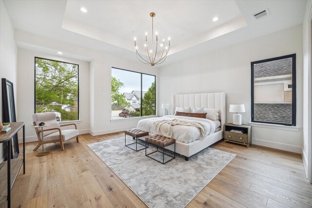 bedroom with a chandelier, visible vents, light wood finished floors, and a raised ceiling