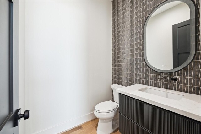 half bath with tile walls, wood finished floors, baseboards, vanity, and toilet