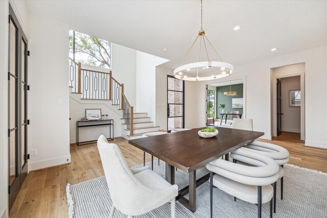 dining space with light wood-type flooring, baseboards, a notable chandelier, and stairway