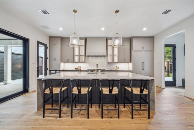 kitchen featuring visible vents, decorative backsplash, wall chimney exhaust hood, light wood-style flooring, and gray cabinetry