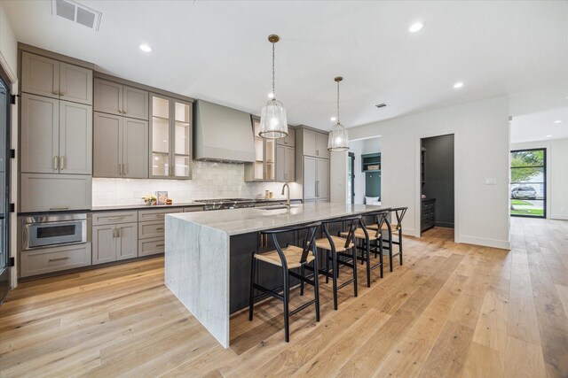 kitchen with custom exhaust hood, a large island, tasteful backsplash, a sink, and gray cabinetry