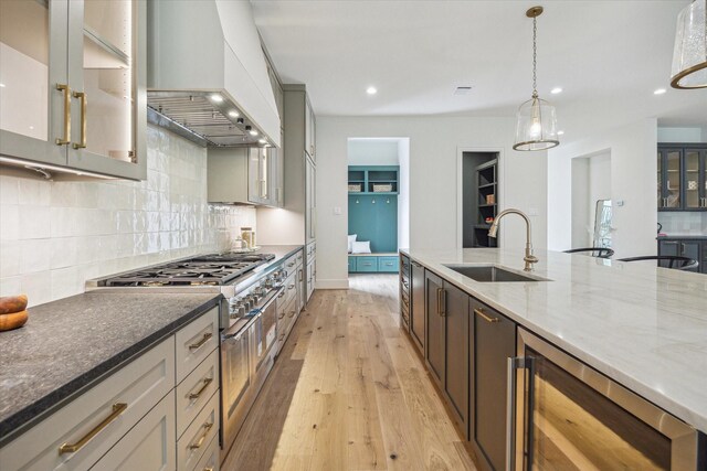 kitchen with a sink, light wood-style floors, beverage cooler, double oven range, and custom range hood